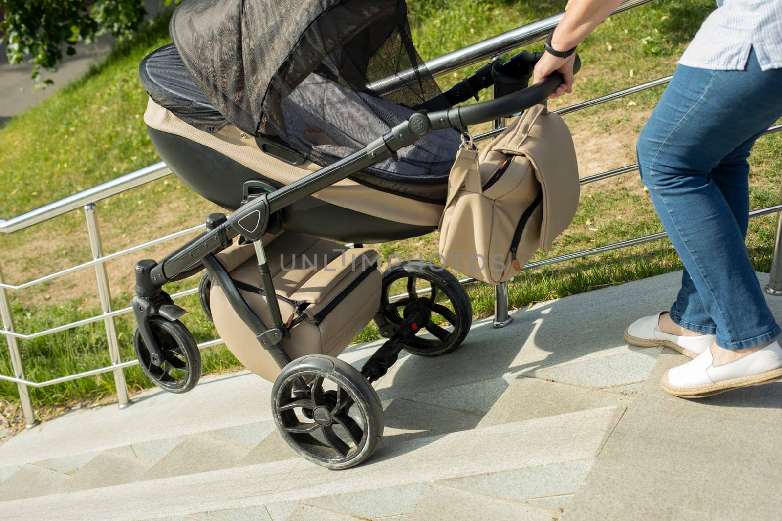 Descent of baby stroller on stairs. Woman lowers stroller with child. Stairs in park. by OlegKopyov