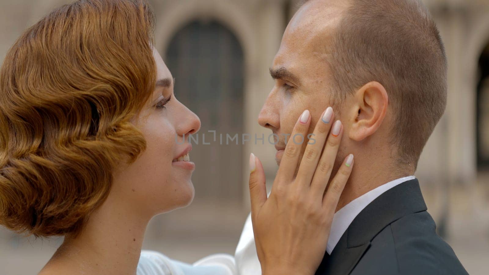 Romantic red haired lady and an elegant gentleman looking at each other with love. Action. Date outdoors on a city background. by Mediawhalestock