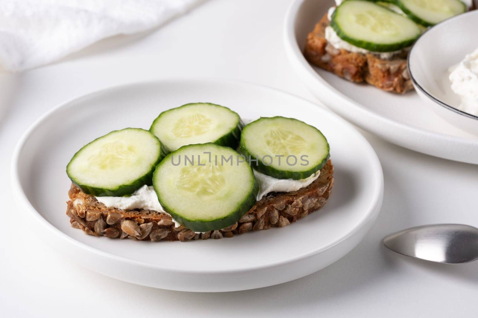 Rye bread with cream cheese and cucumbers on a white table. Whole grain rye bread with seeds.