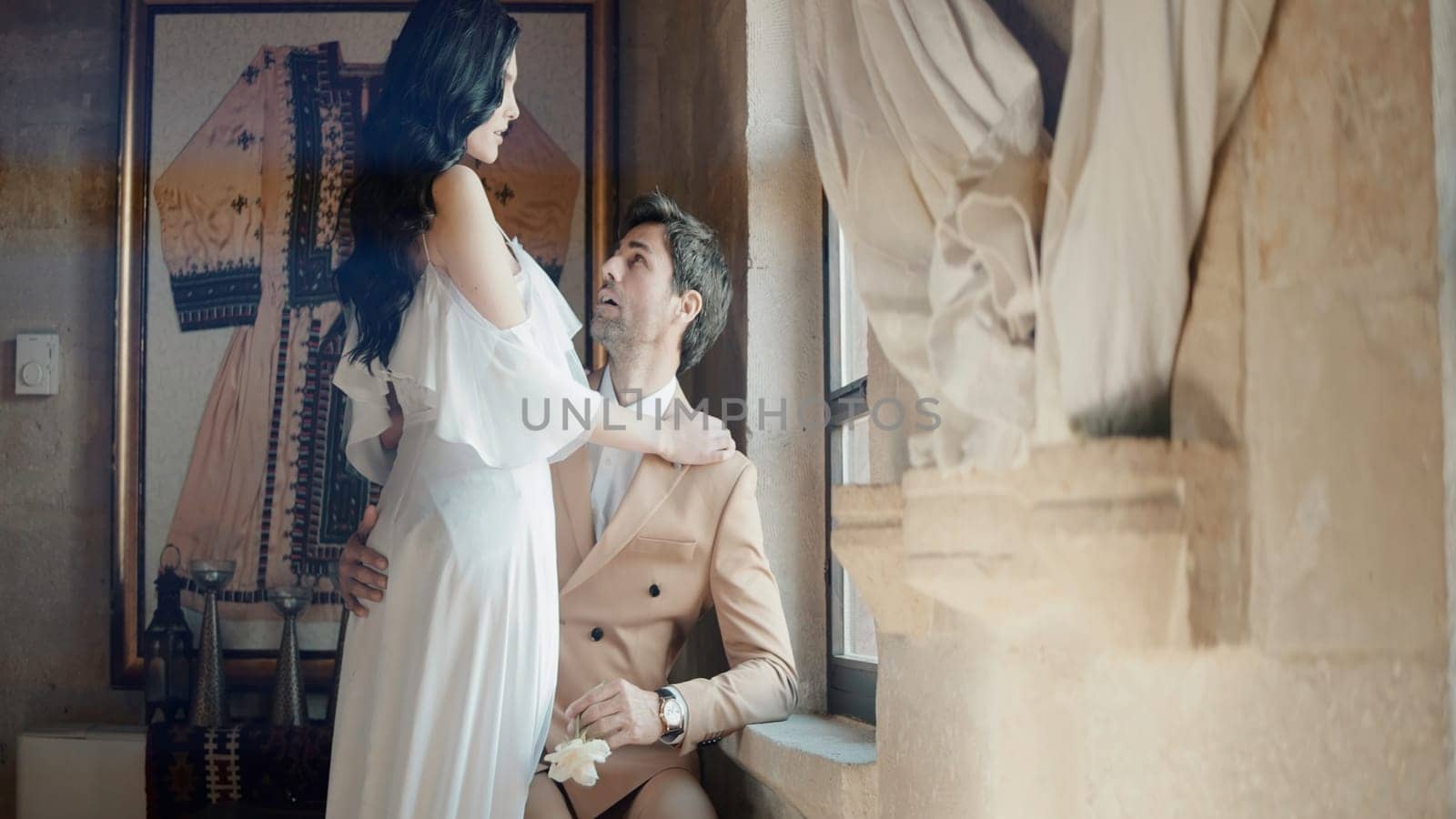 Beautiful fashionable studio shooting . Action . A beautiful young couple in wedding costumes, a bride in a magnificent dress, who are sitting on the floor in a stone room with various decorations on the walls and lighting from below. High quality 4k footage