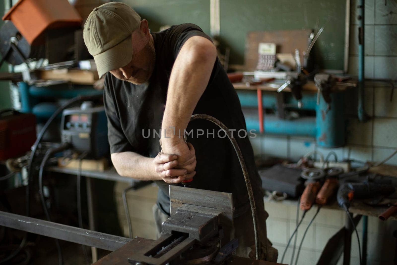 Guy in garage is repairing steel part. Man grinds iron. by OlegKopyov