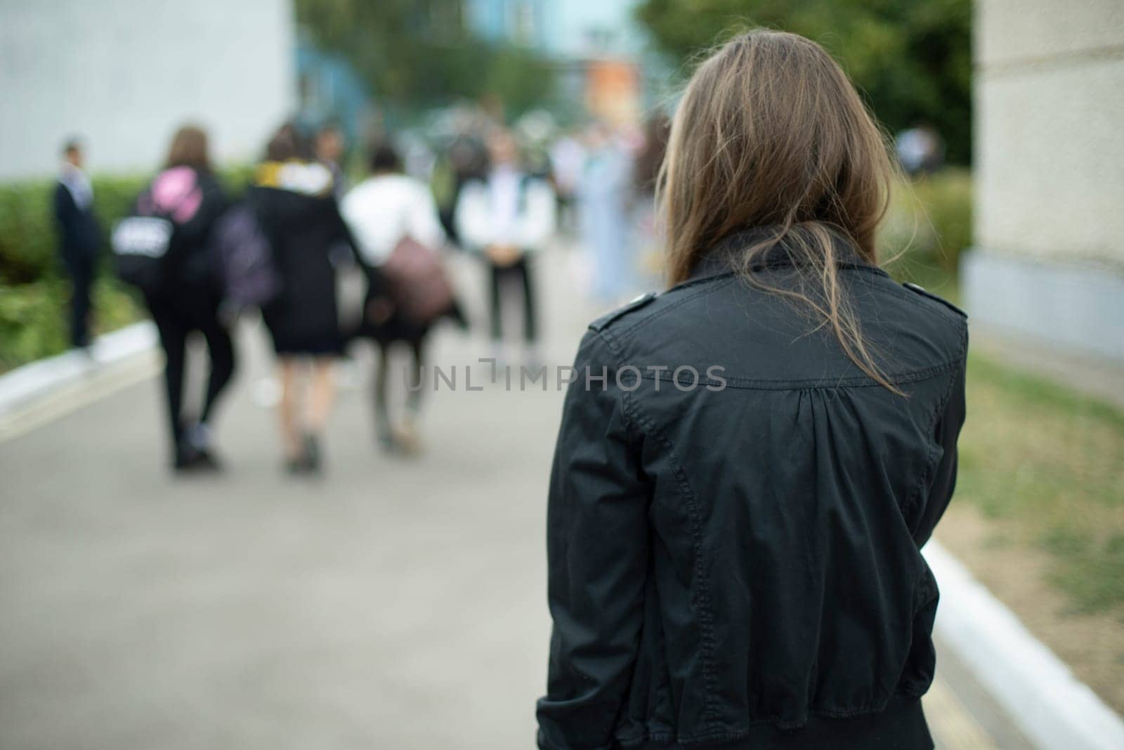 Girl in black jacket in schoolyard. Girl is coming home from school. Black clothes. Fashion details.
