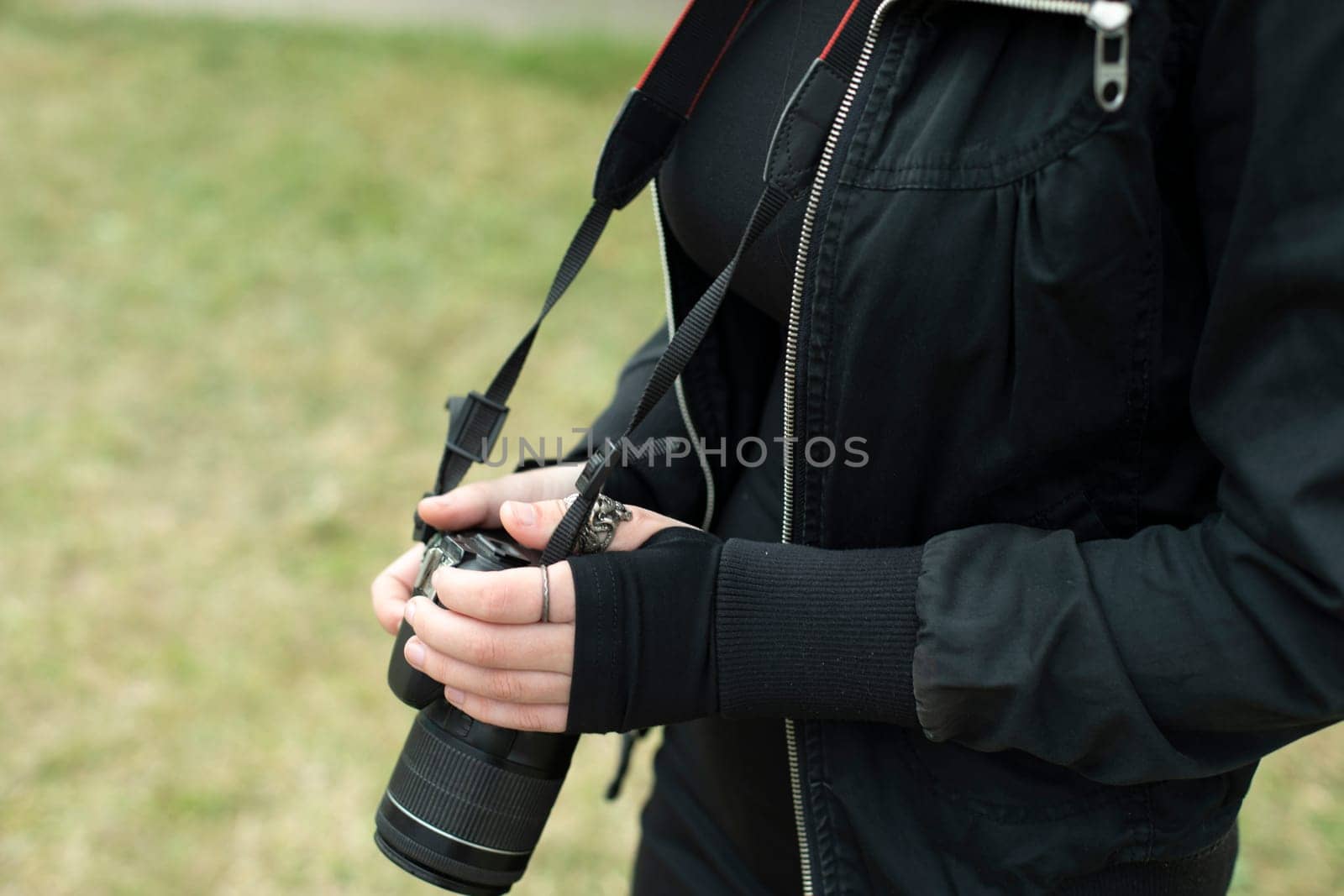 Girl with camera in black clothes. Hands hold camera. Clothing details. Photo correspondent on street.