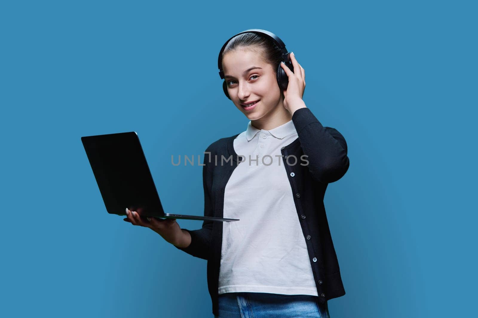 Teen girl student wearing headphones using laptop, on blue background by VH-studio