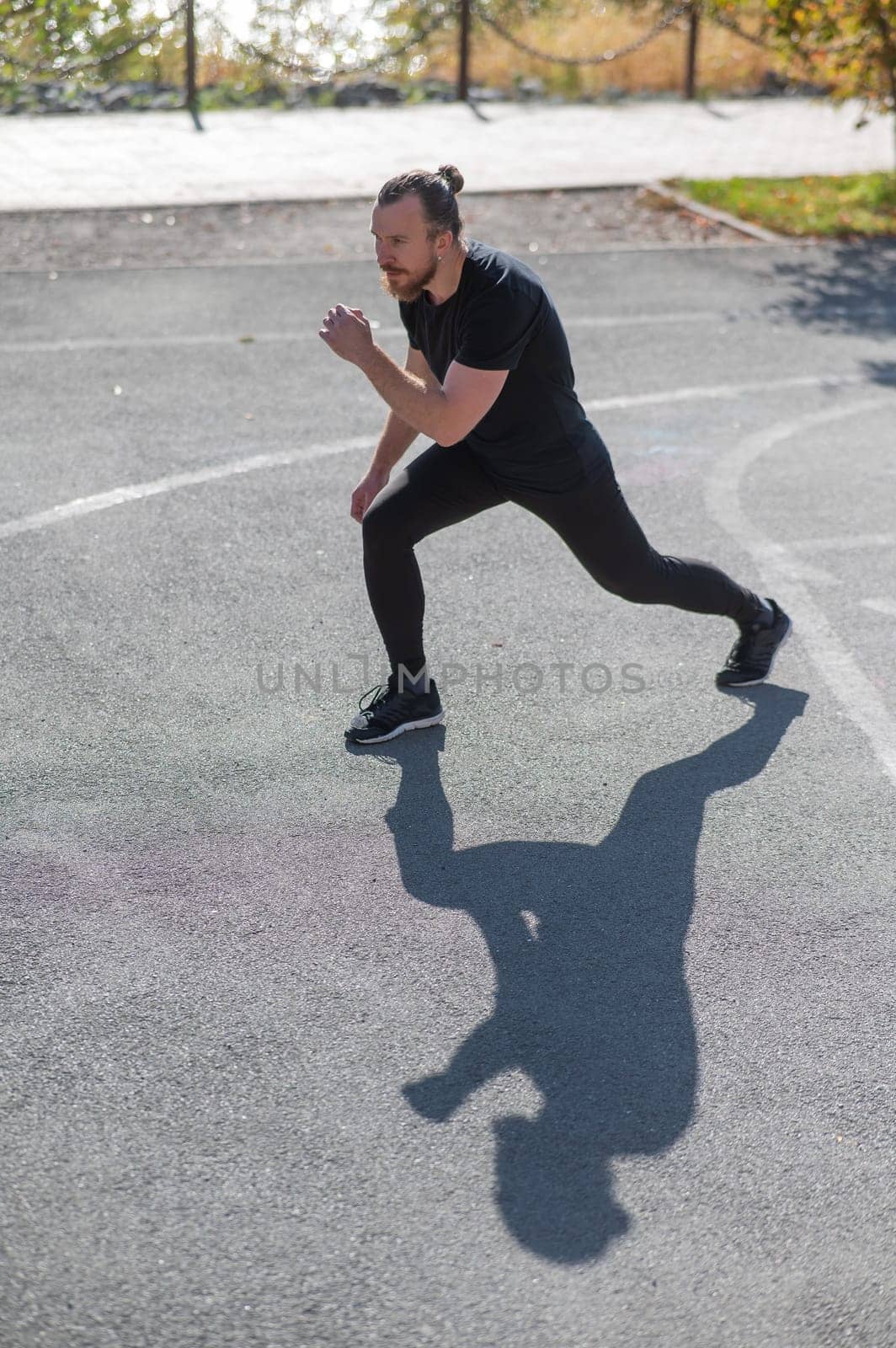 Bearded man with long hair doing lunges on the sports field. by mrwed54