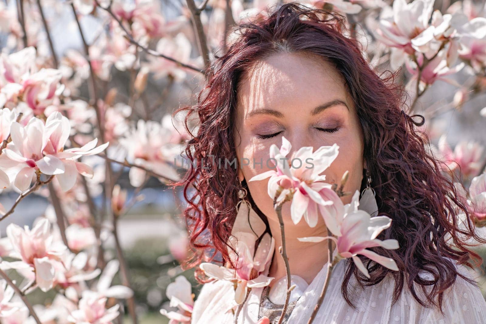 Magnolia park woman. Stylish woman in a hat stands near the magnolia bush in the park. Dressed in white corset pants and posing for the camera. by Matiunina