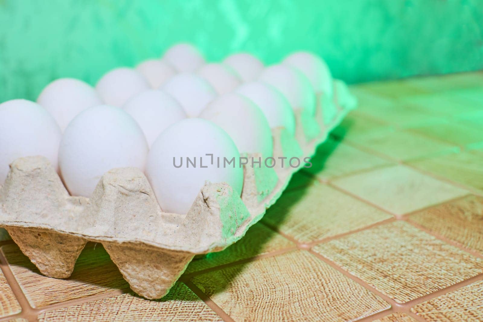 Chiken white eggs in a cardboard tray on a green back wall by jovani68