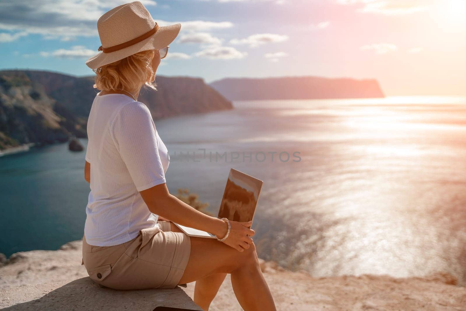 Freelance women sea working on the computer. Good looking middle aged woman typing on a laptop keyboard outdoors with a beautiful sea view. The concept of remote work