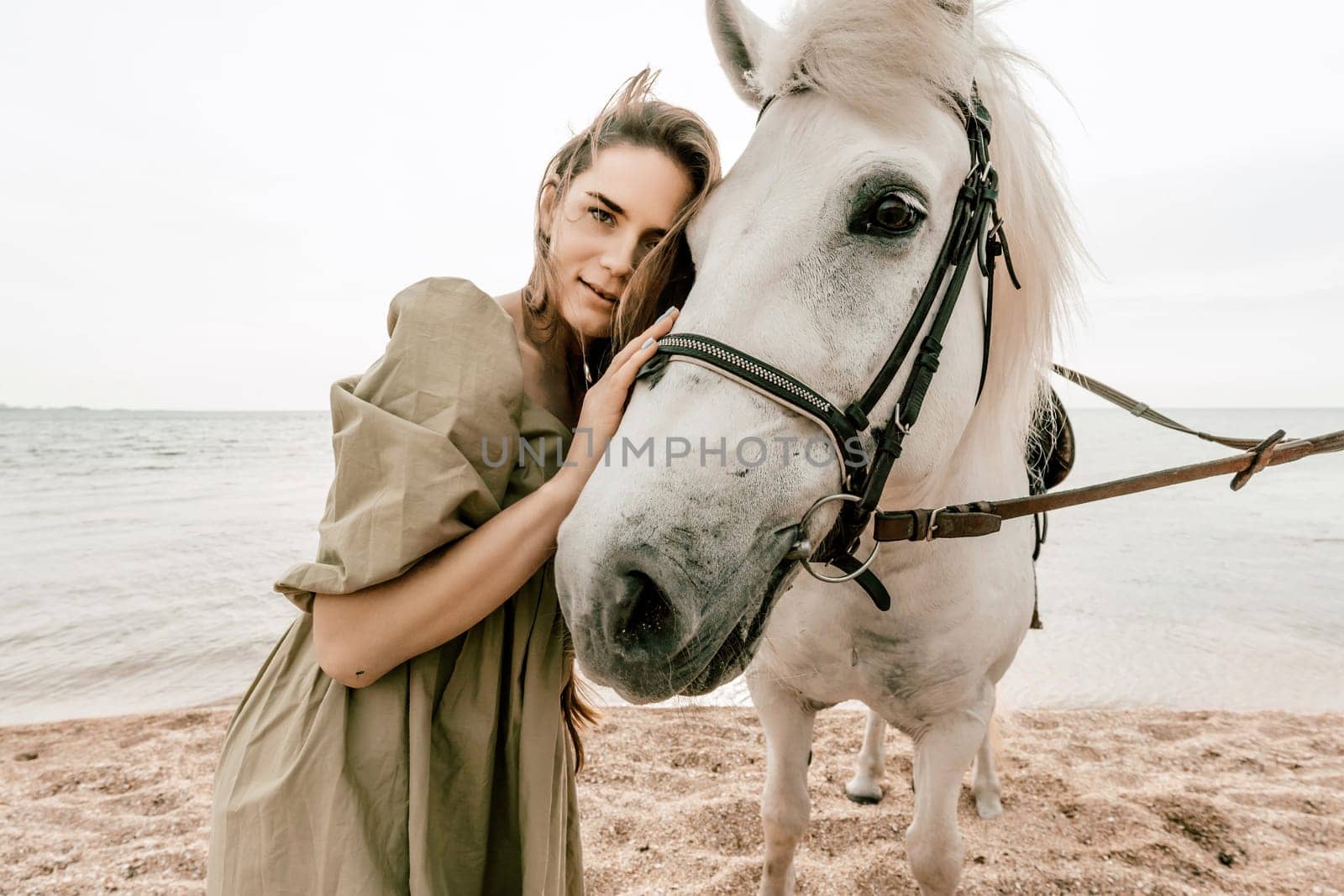 A woman in a dress stands next to a white horse on a beach, with the blue sky and sea in the background