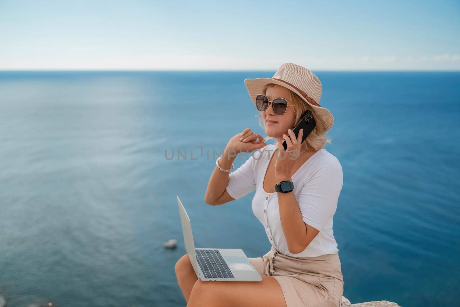 Freelance women sea working on the computer. Good looking middle aged woman typing on a laptop keyboard outdoors with a beautiful sea view. The concept of remote work