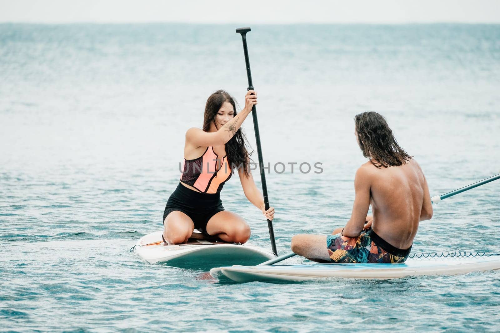 Sea woman and man on sup. Silhouette of happy young woman and man, surfing on SUP board, confident paddling through water surface. Idyllic sunset. Active lifestyle at sea or river