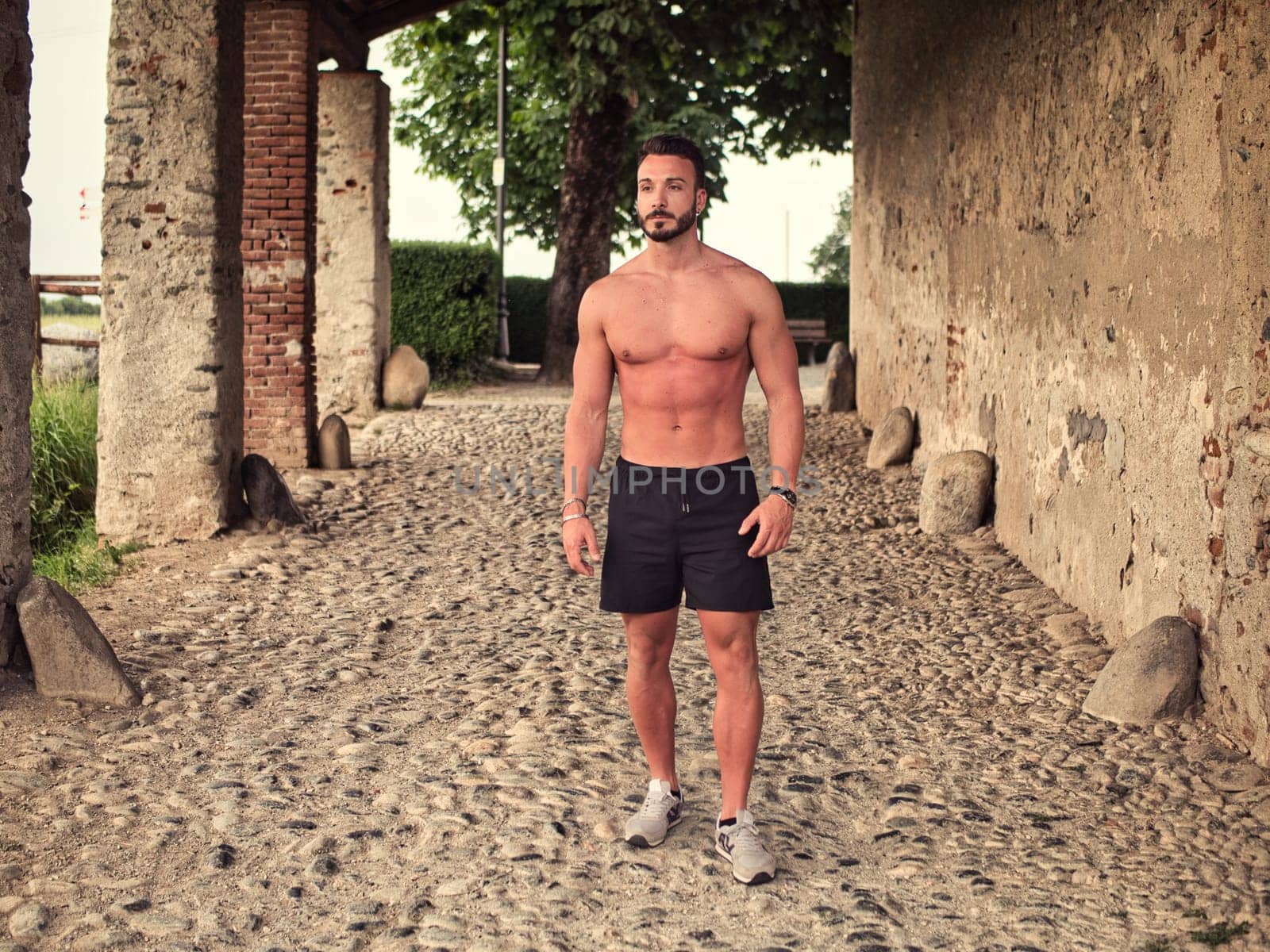 A shirtless man standing in an alley way. Confident Athlete Demonstrating Strength in Front View Portrait