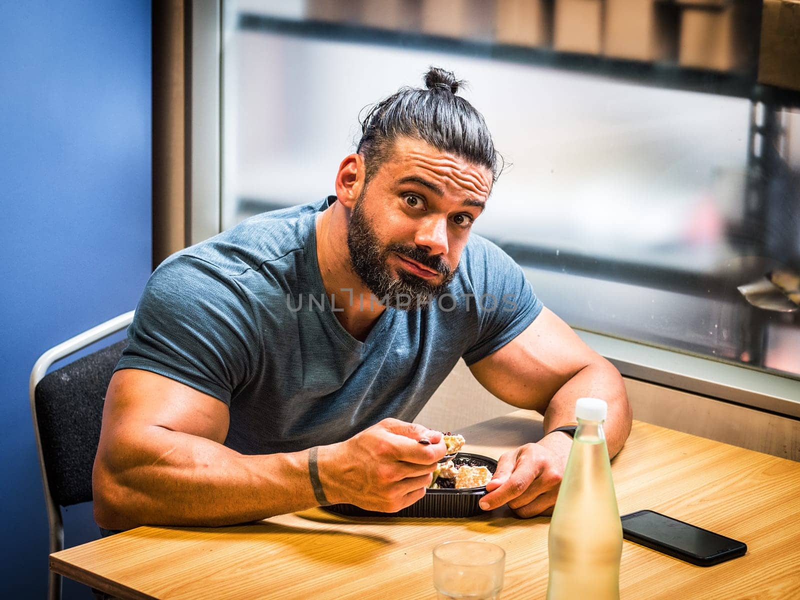 A man sitting at a table with a plate of food. Photo of a man having a meal at a table, looking at camera disappointed