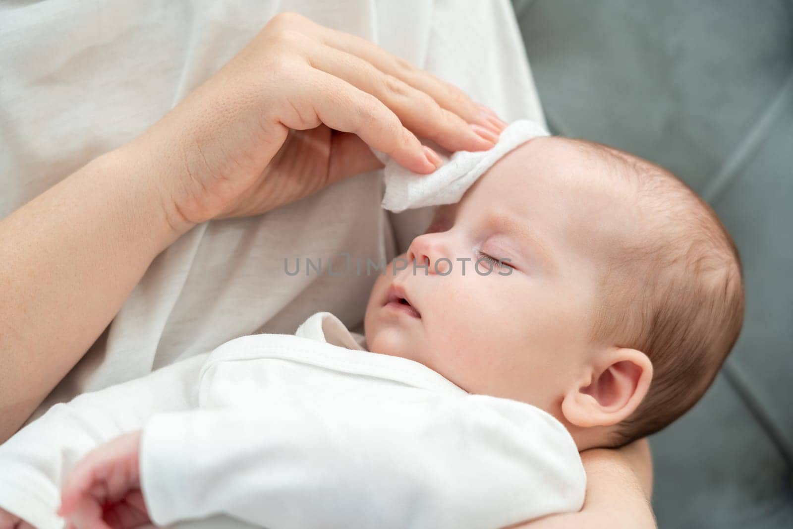 Holding her unwell baby, a mother tenderly touches the newborn's forehead using a wet wipe