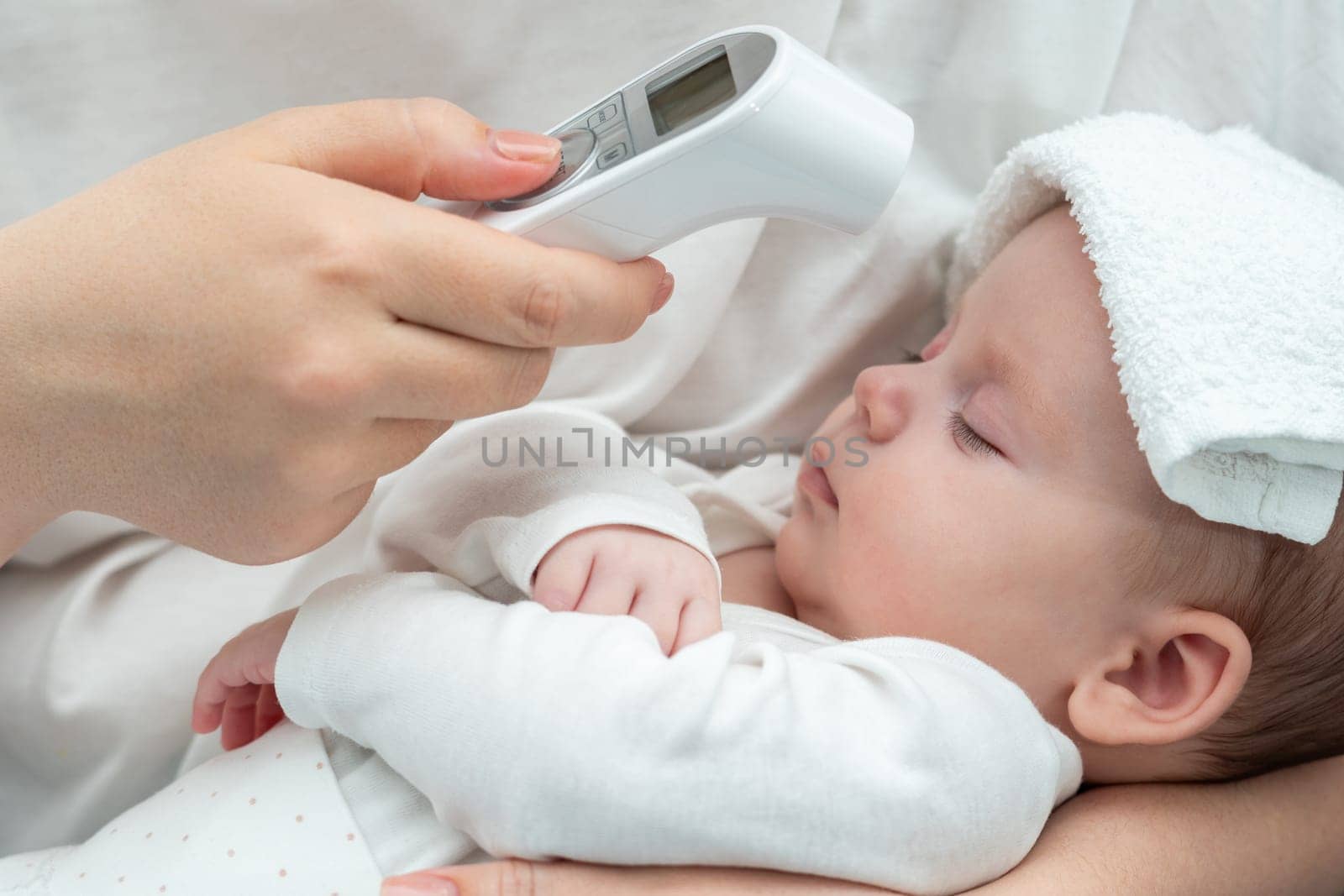 Mother attentively uses an electronic thermometer to measure her newborn baby's forehead