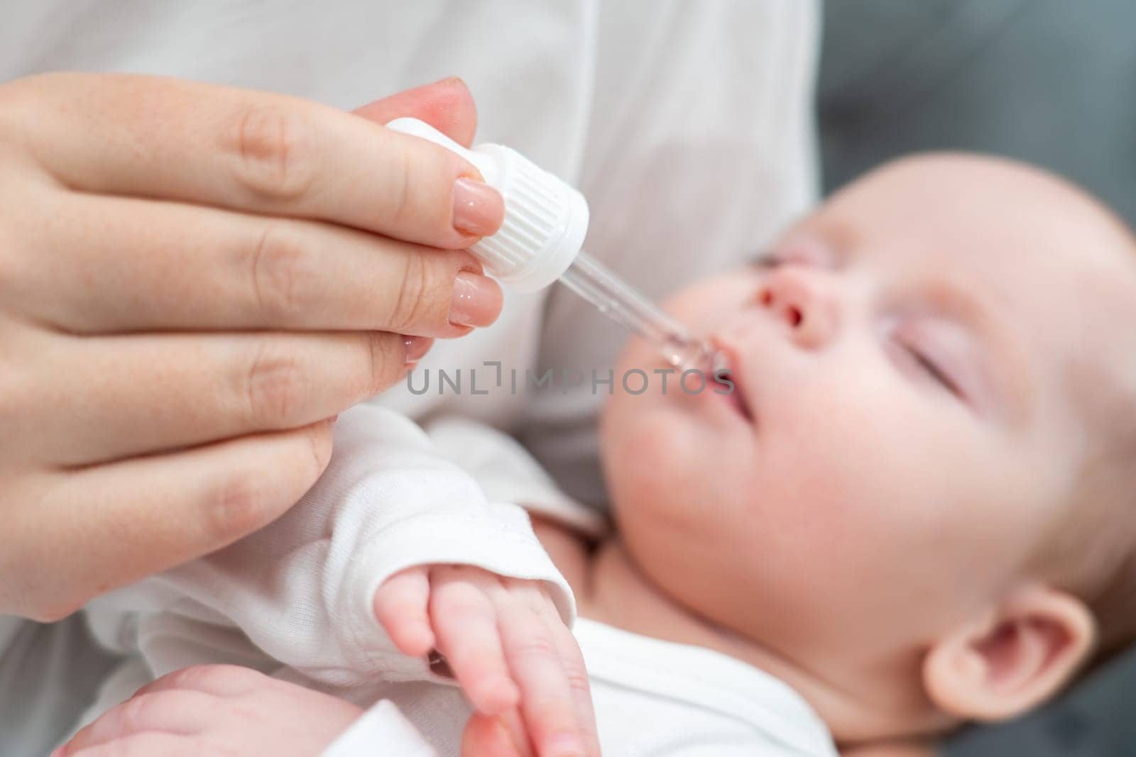 While cradling her sleeping baby, mother gently buries oral drops using a pipette ensuring utmost