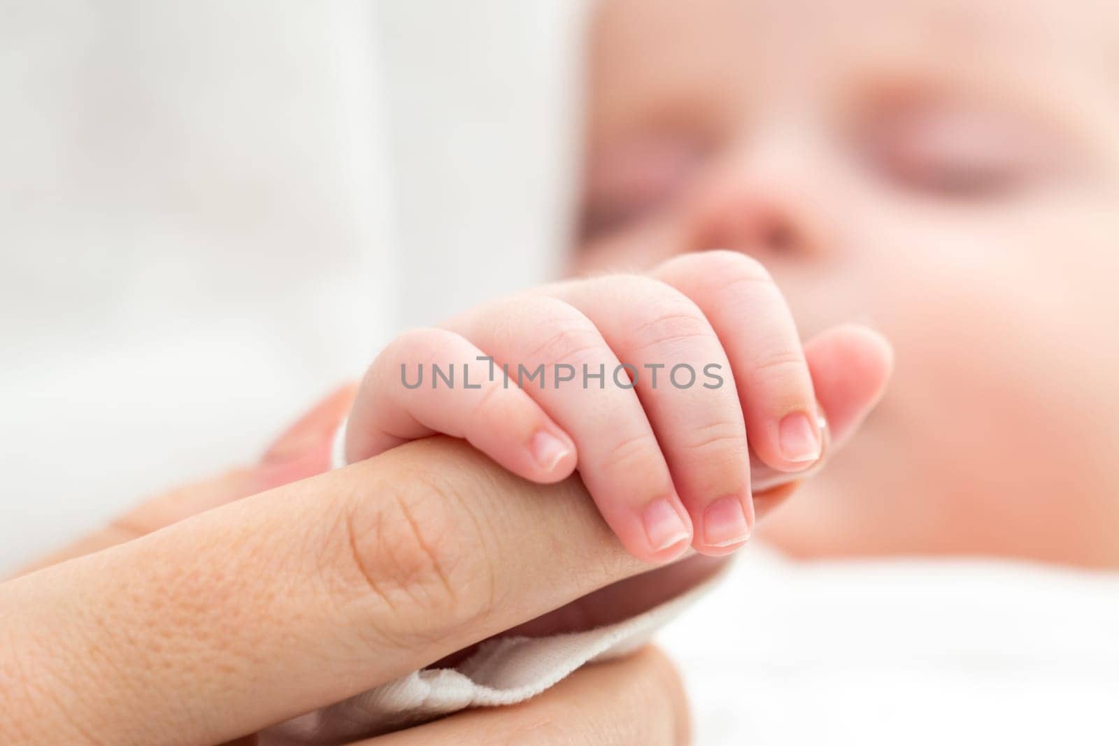 Newborn's tiny hand clutches mother's finger. Concept of maternal bond and love by Mariakray