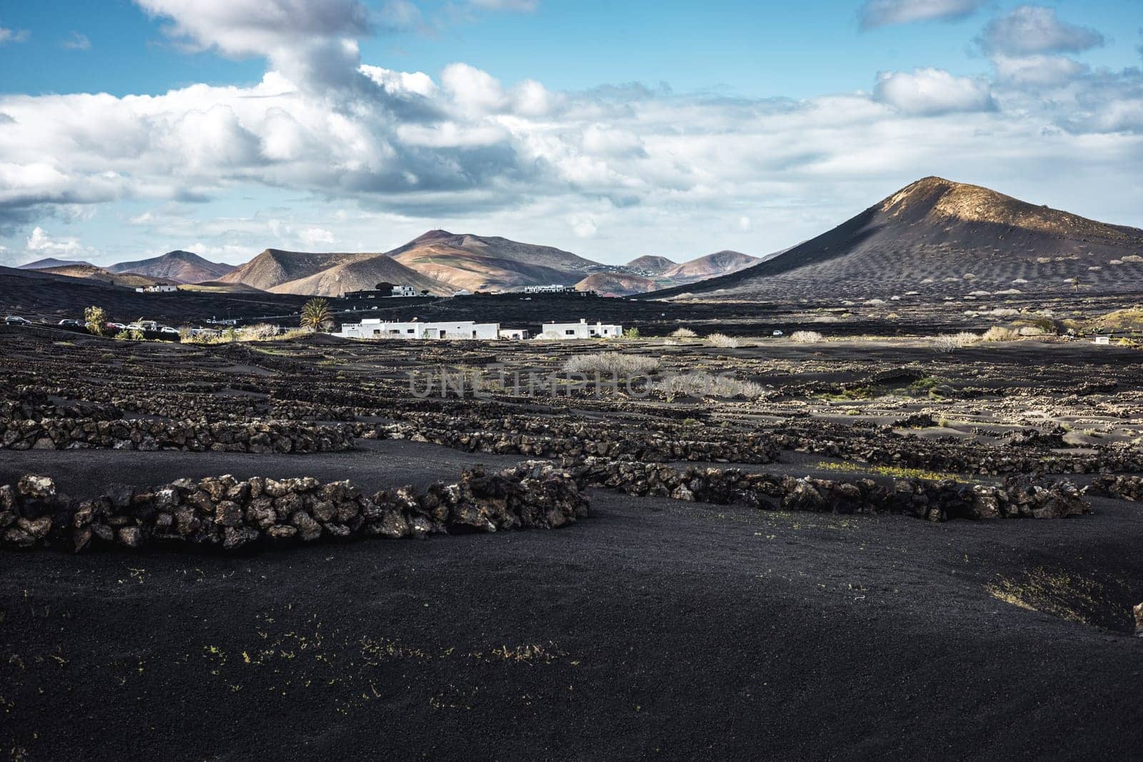 Traditional white houses in black volcanic landscape of La Geria wine growing region with view of Timanfaya National Park in Lanzarote. Touristic attraction in Lanzarote island, Canary Islands, Spain