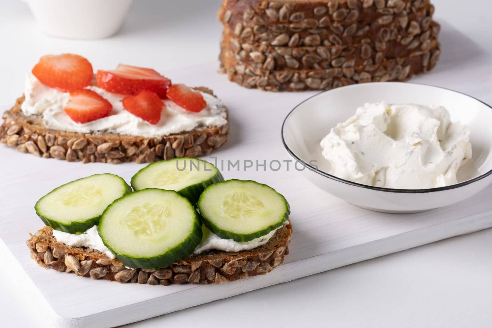 Rye bread with cream cheese and cucumbers, strawberry on a white table. Whole grain rye bread with seeds.