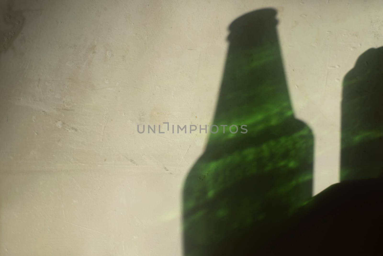 Light on wall from bottle of beer. Green glass and shadow on wall. Silhouette of bottle of beer.