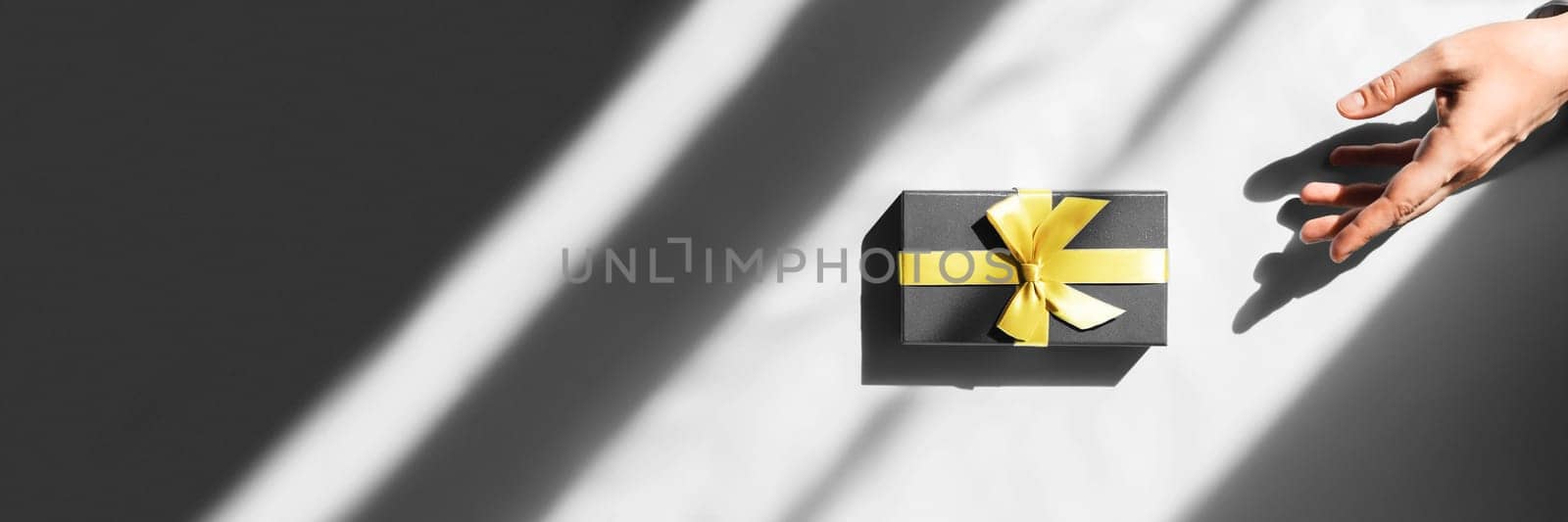 Girl in sunlight pulls her hand behind box with gift of bandaged yellow ribbon.