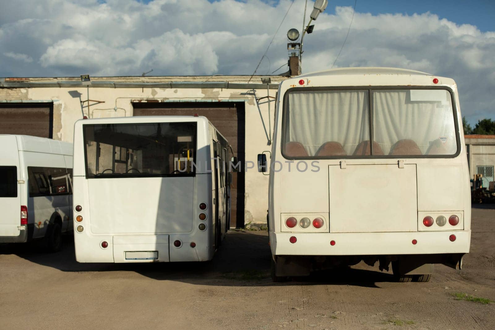 Parking of vehicles. Buses are white. Private area with buses. Place for cars.