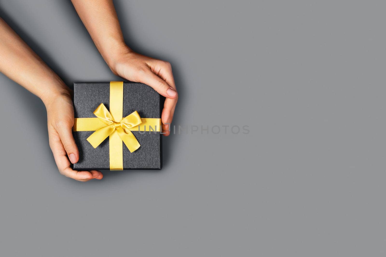 Girl holds gift bandaged with yellow ribbon on gray background.