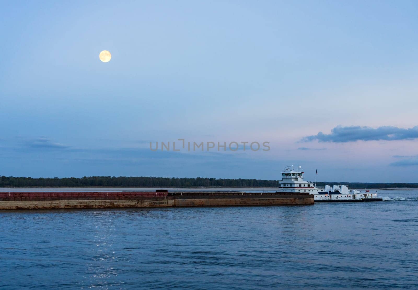 Large river barge loaded with grain sailing down Mississippi river near Natchez at dusk