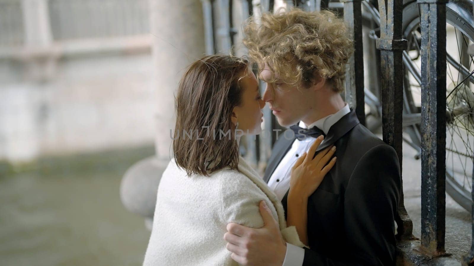 Passionate bride and groom embracing by the iron gate. Action. Sexy young man and woman in suit and white dress in windy weather