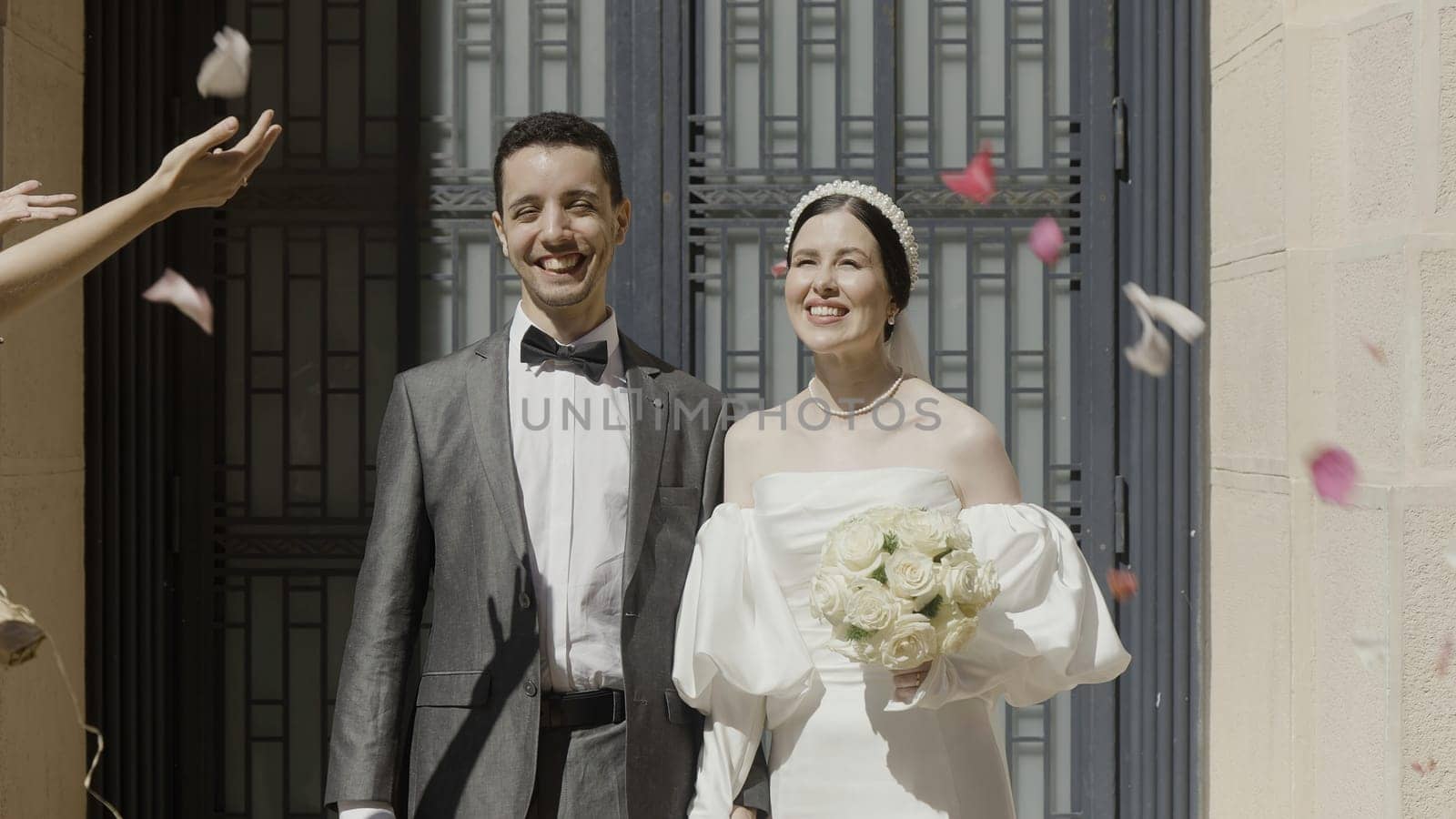A wedding party with happy faces. Action. The newlyweds on whom the rose petals are thrown pose and smile brightly next to the registry office. High quality 4k footage