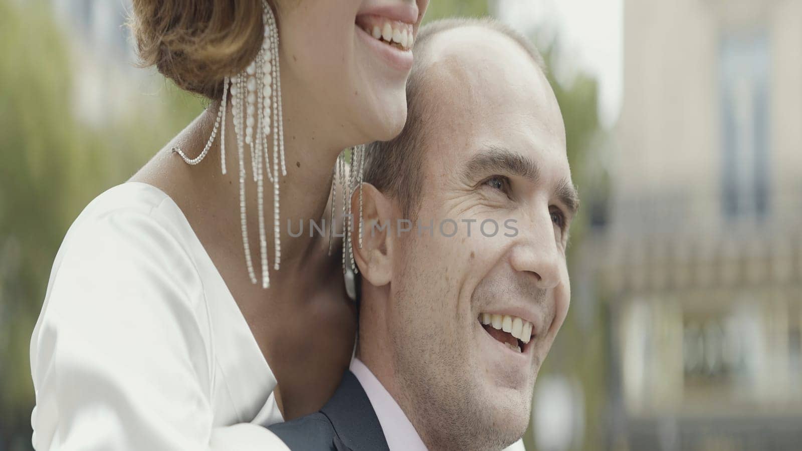 Close up of lovely couple together in slow motion outdoors. Action. Romantic couple hugging, wearing suit and white dress with long attractive earring