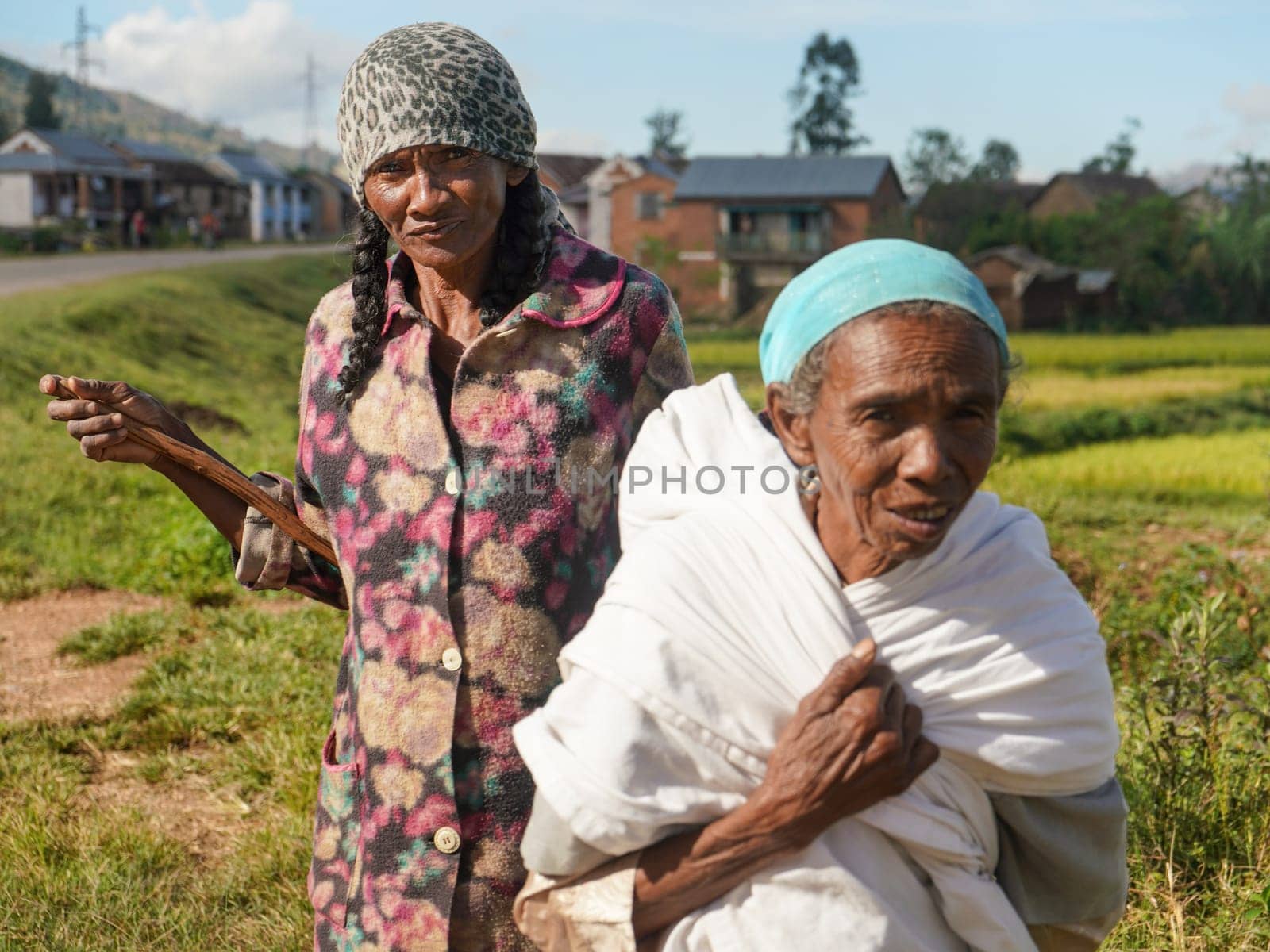 Manandoana, Madagascar - April 26, 2019: Unknown senior Malagasy women standing next to rice field where they worked on sunny day. People in this part of Africa are poor, but cheerful.