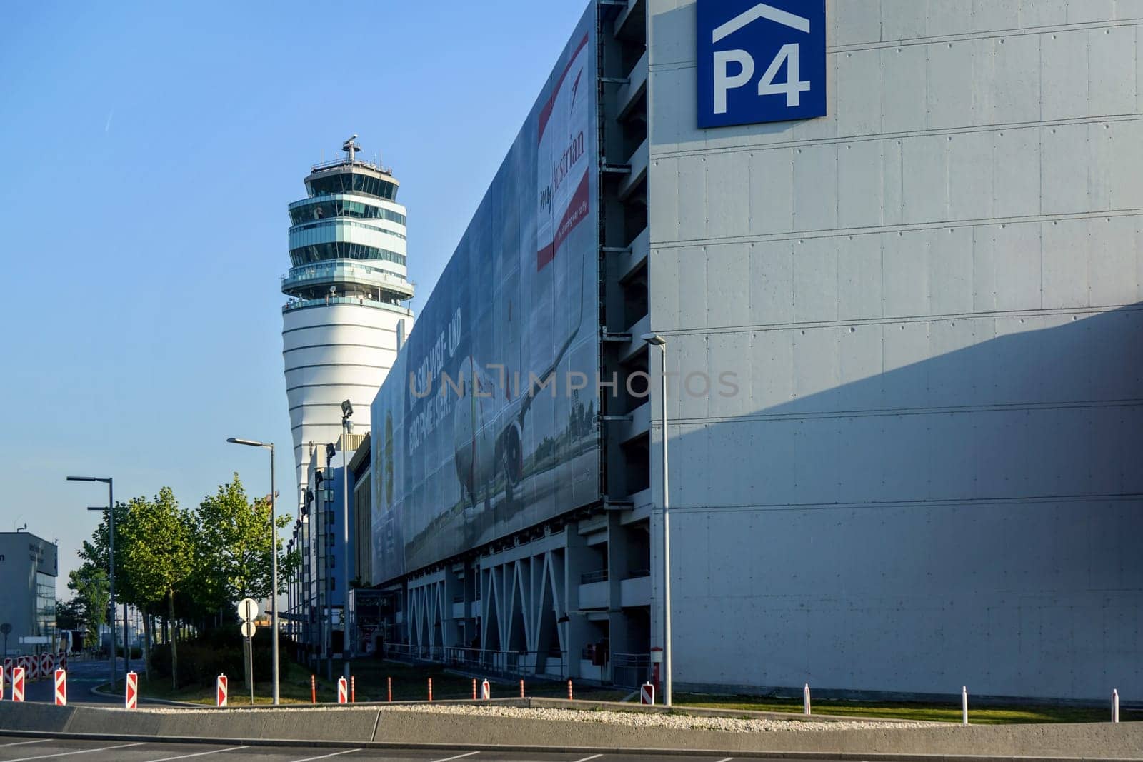 Schwechat, Austria - May 08, 2019: Main tower of Vienna international airport with parking building on the right side with Austrian airlines (which has main base at Vienna) banner on wall by Ivanko