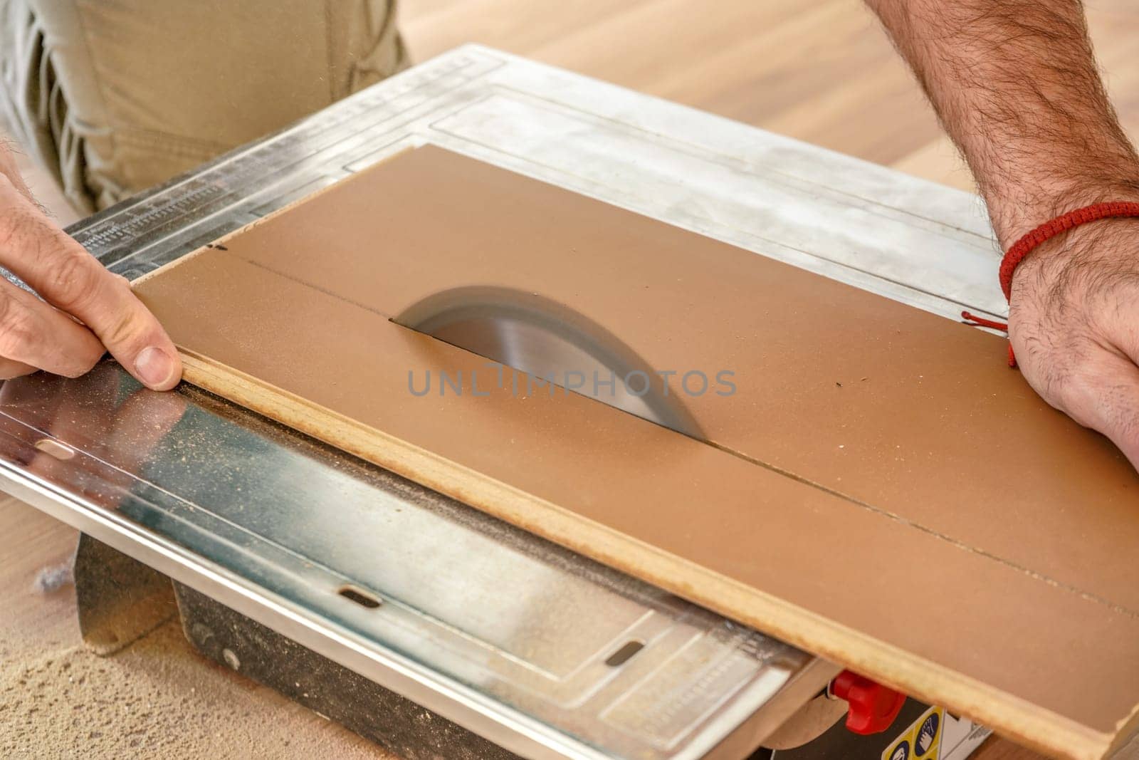 Man cutting laminate floor boards on circular saw, detail on hands holding wooden panel and rotating ring, home improvement illustration photo