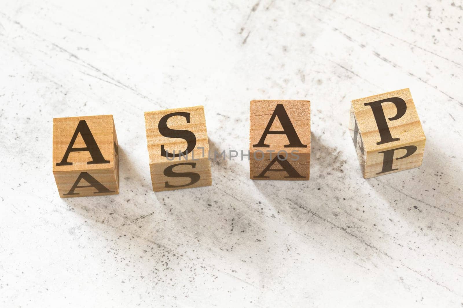 Four wooden cubes with letters ASAP (meaning As soon as possible) on white working board.