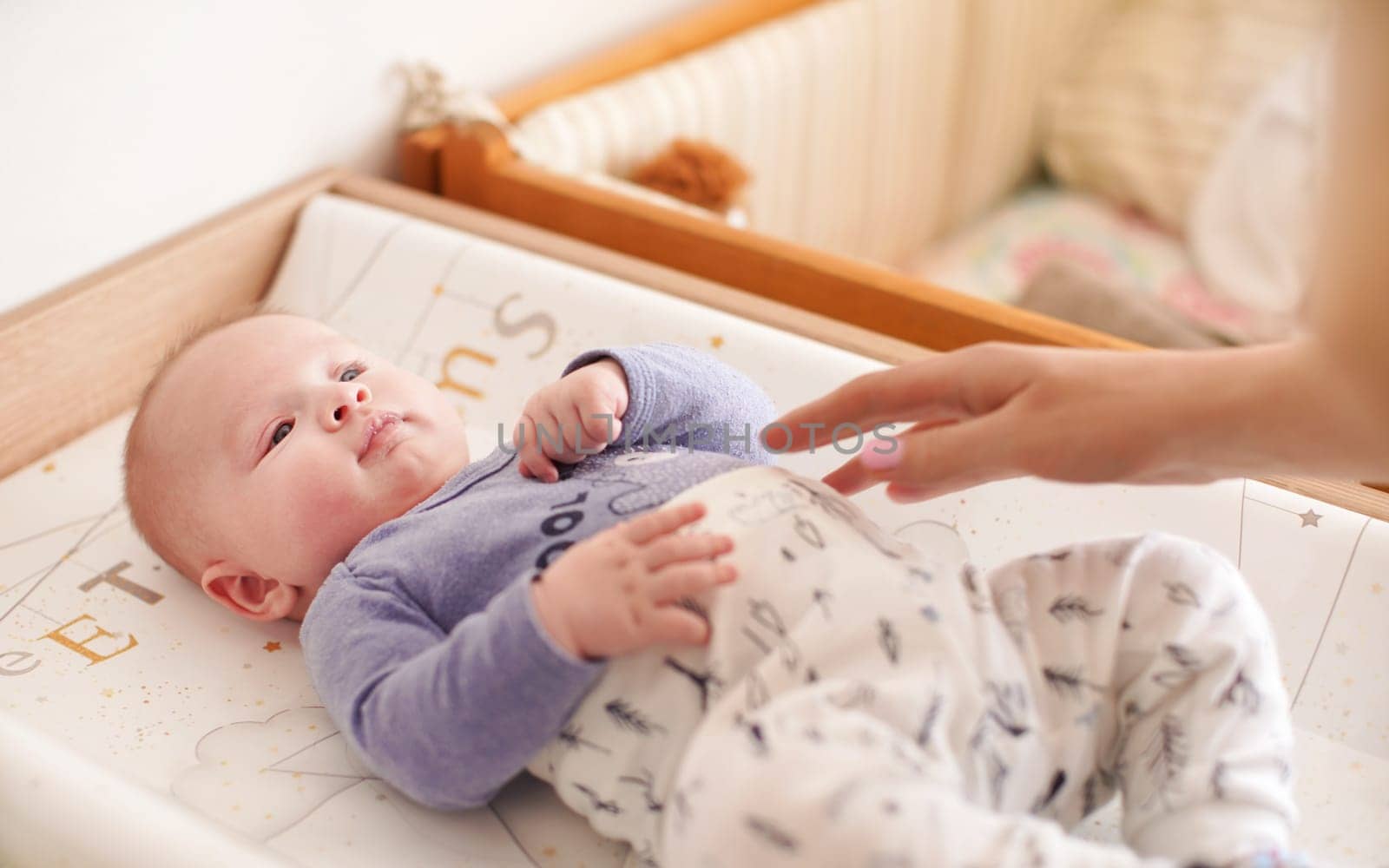 Four months old baby boy laying in bed ready for changing clothes, mother hands over him