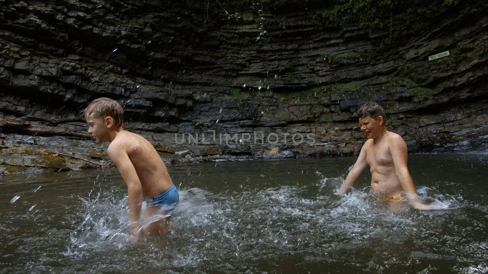 Young boys bathing in a small lake within the mountain. Creative. Little boys splashing cold water