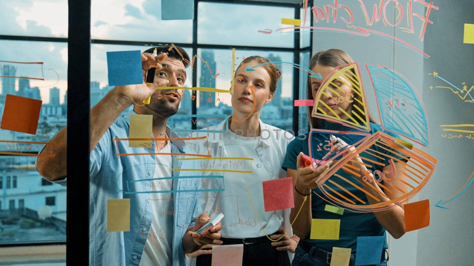 Professional business team brainstorm, sharing, thinking idea while skilled male leader write on sticky notes at glass wall. Skilled manager placed business plan on glass wall at office. Tracery