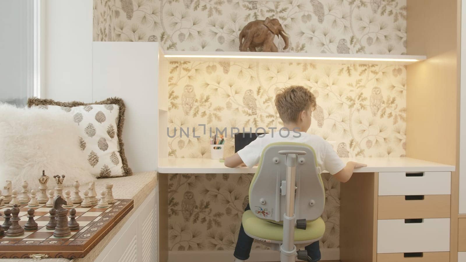 Interior of children's room with boy sitting at table. Creative. Boy is studying at desk. Children's room of smart boy studying at table.