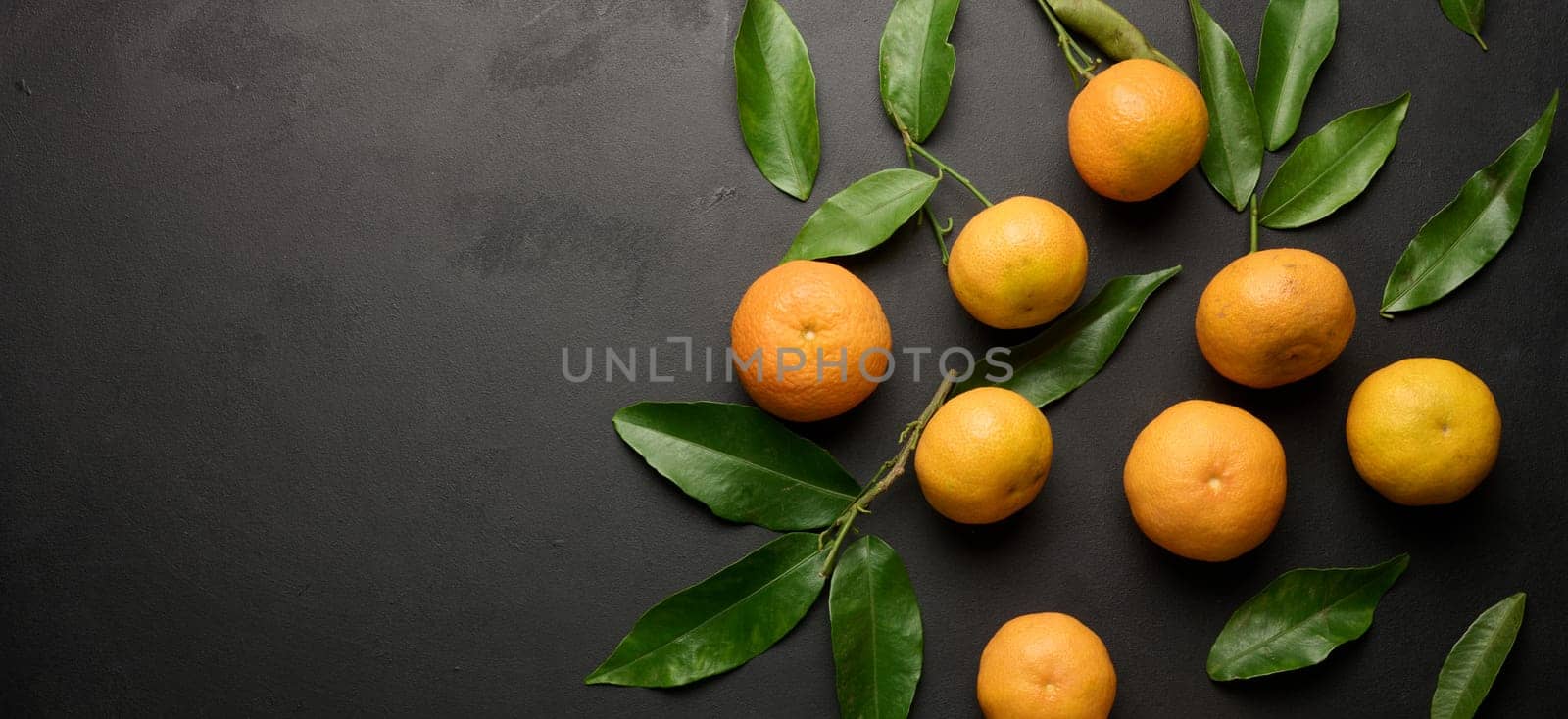 A ripe clementine with green leaves on a black table, top view. Copy space
