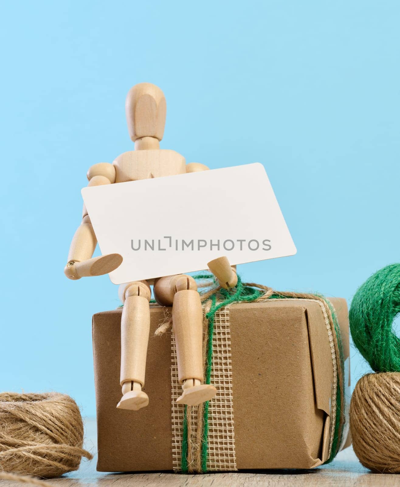 Wooden mannequin holding a white paper business card and gifts wrapped in brown craft paper on a blue background by ndanko