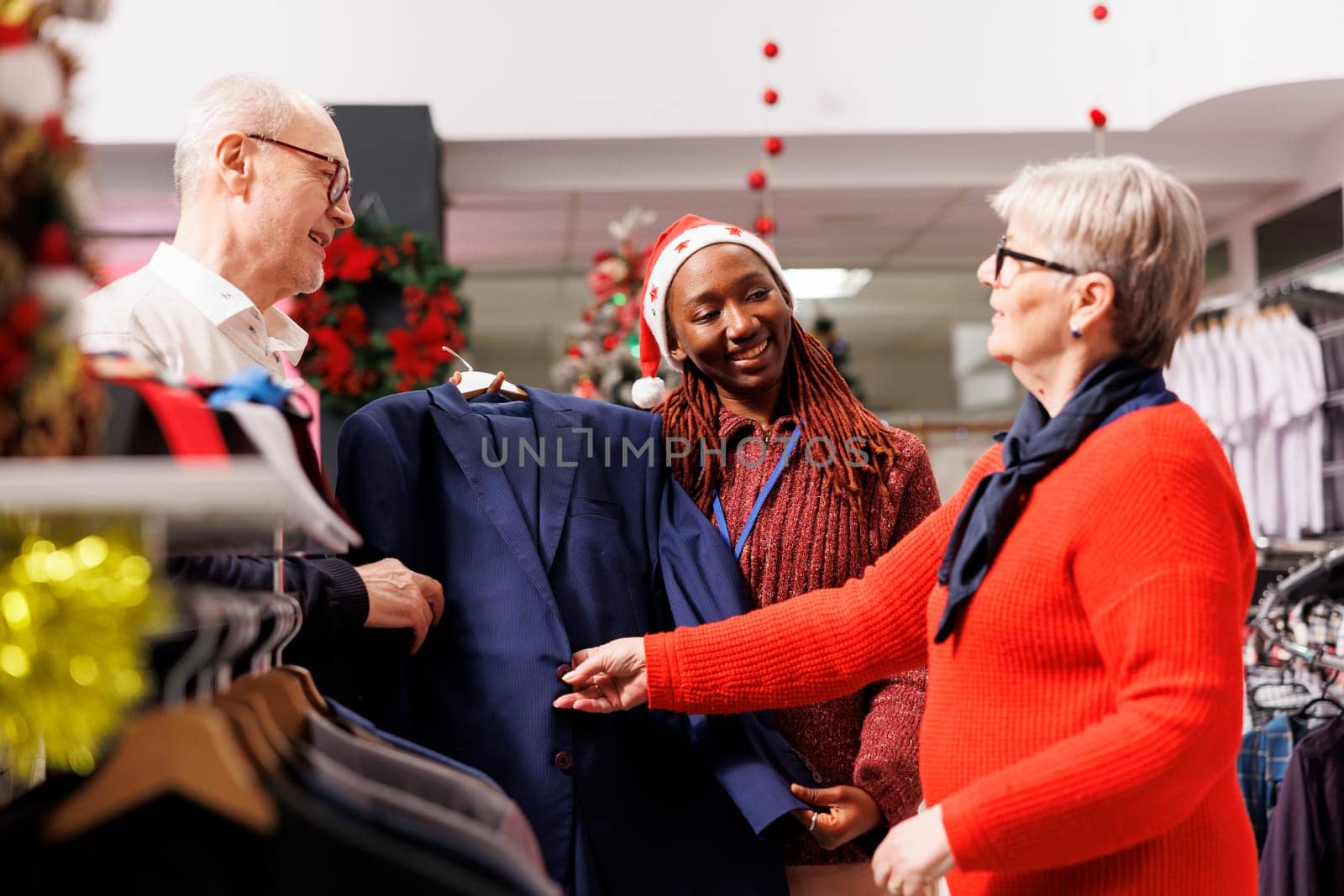 Sales assistant holding suit jacket for senior people, recommending perfect clothes for christmas eve outfit. Woman store employee helping clients buy formal attire, presenting merchandise.