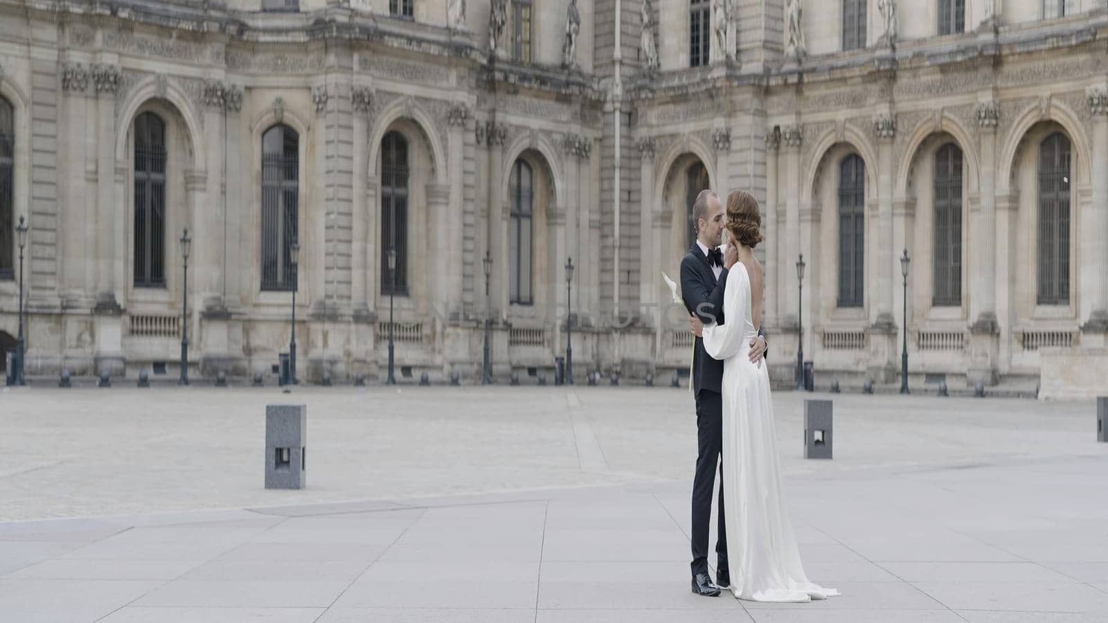 Newlyweds with an antique building on the background. Action. Beautiful bride and groom look each other and kiss