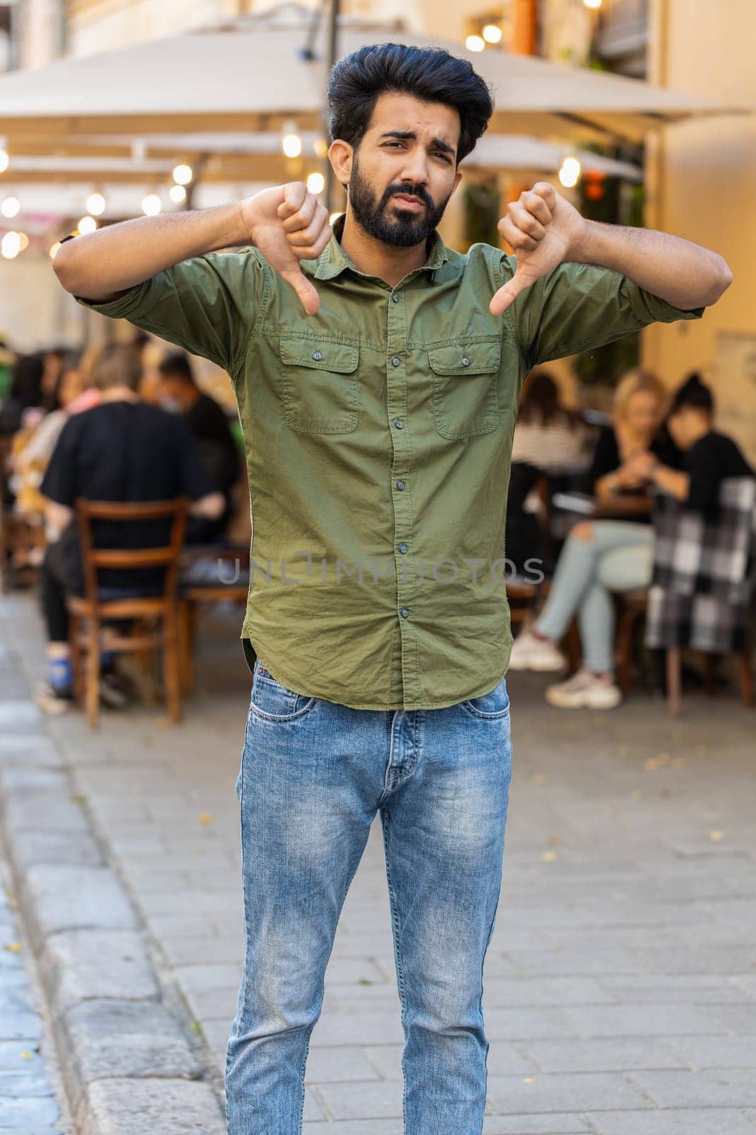 Dislike. Upset bearded indian man showing thumbs down sign gesture, expressing discontent, disapproval, dissatisfied bad work, mistake. Displeased guy standing in urban city sunshine street. Vertical