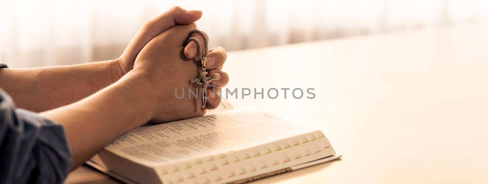 Asian male folded hand prayed on holy bible book while holding up a pendant crucifix. Spiritual, religion, faith, worship, christian and blessing of god concept. Blurring background. Burgeoning.