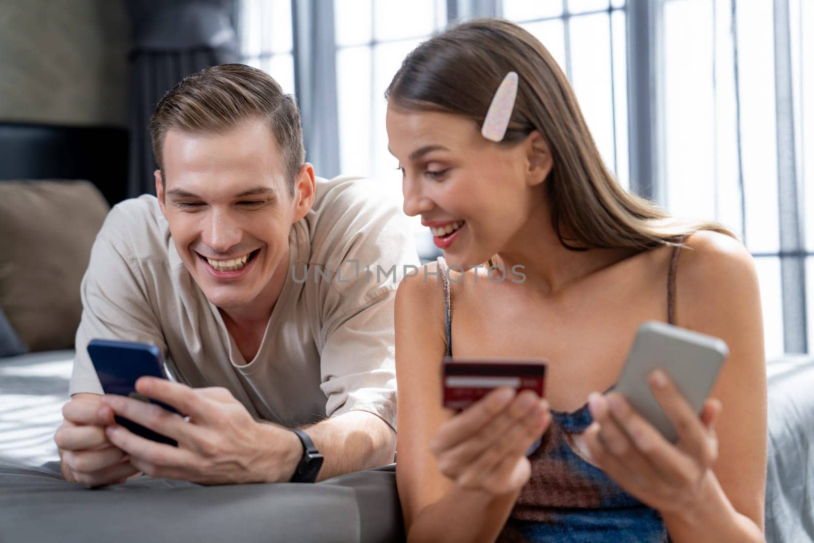 Young couple sit in the bed room using online payment app. Unveiling by biancoblue