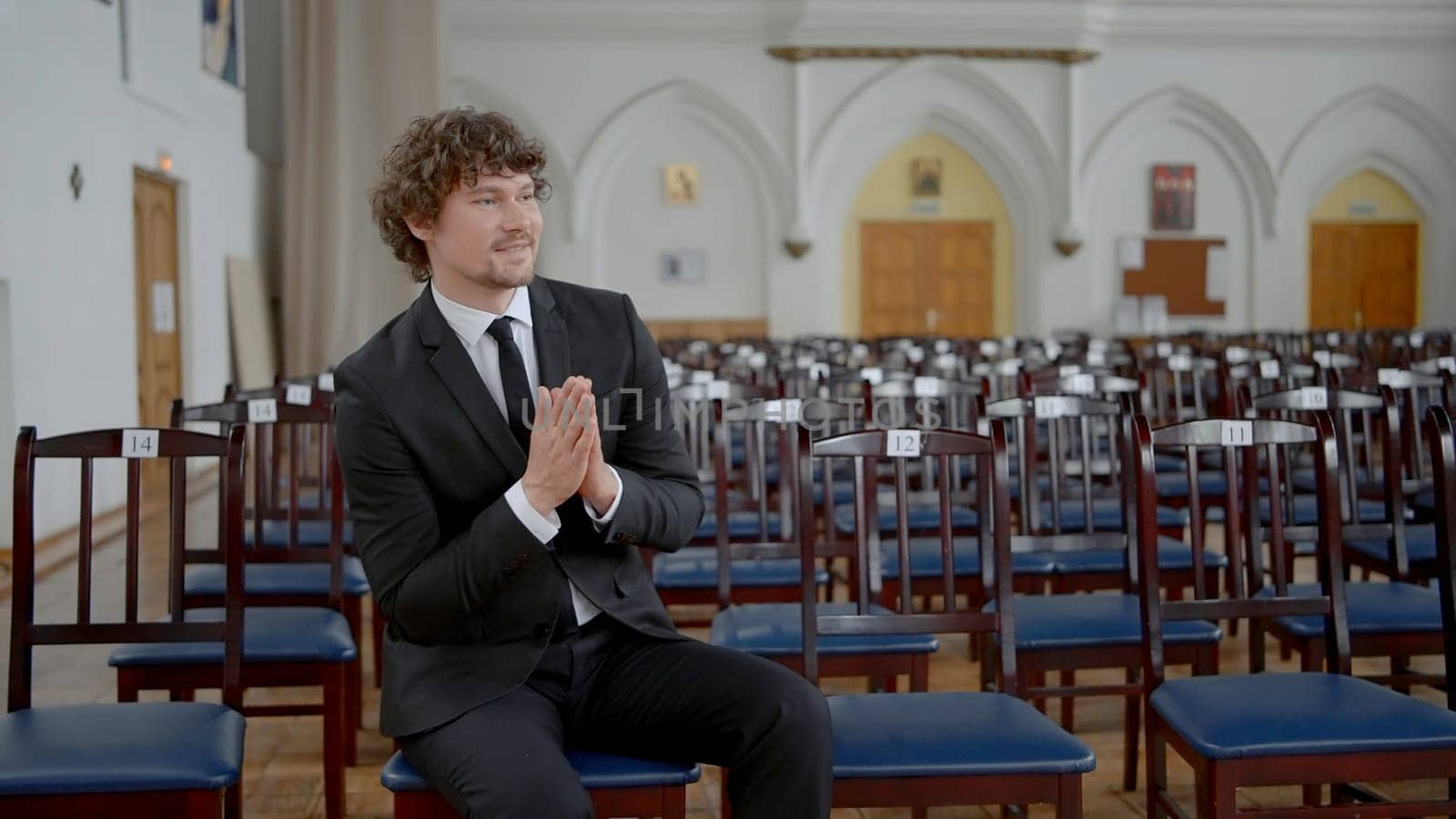 Groom in empty church. Action. Attractive man in suit is sitting alone in church. Groom is sitting alone and waiting for preparation of wedding ceremony. Rehearsal of wedding ceremony in temple.