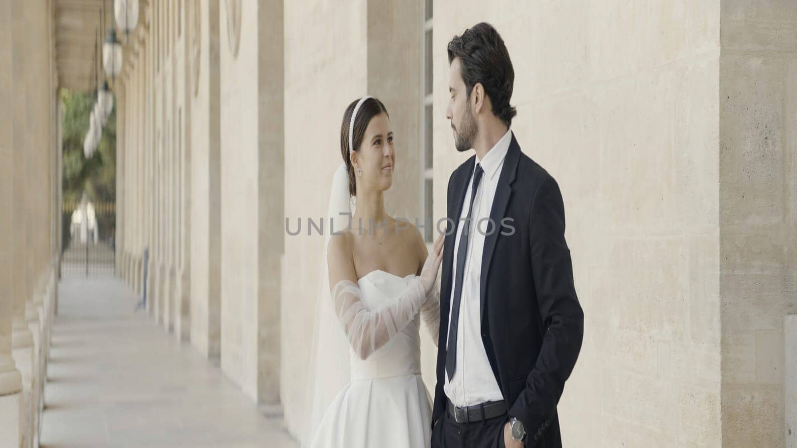 Man and woman in wedding clother stand near the big pillars. Action. Young and beautiful couple on their wedding day