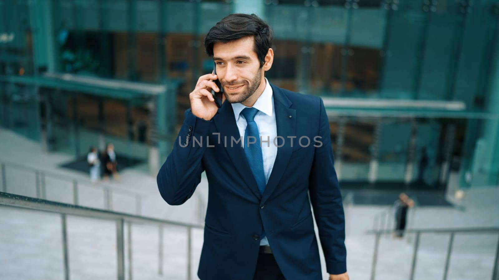 Skilled caucasian project manager calling phone while walking at city with blurred background. Skilled businessman using smart phone talking to project manager with blurred background. Exultant.