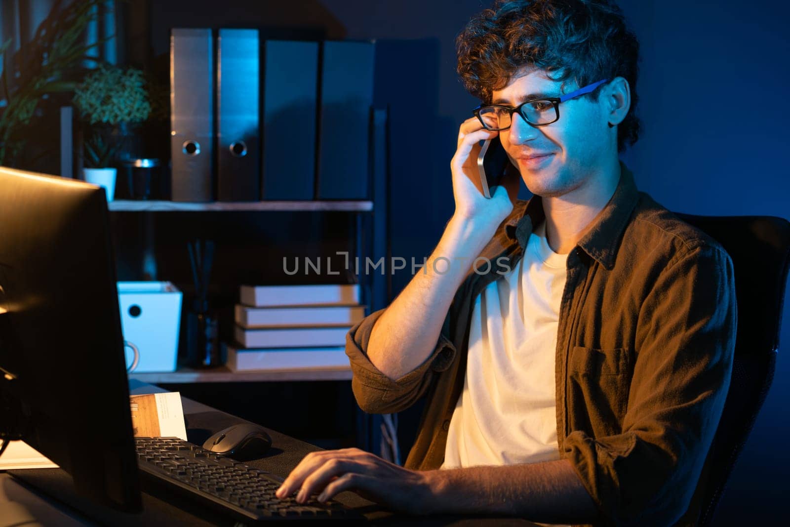 Young businessman calling on smartphone to customer or coworker, looking at computer screen of creative presentation surround work desk at neon modern office. Concept of new next project. Gusher.